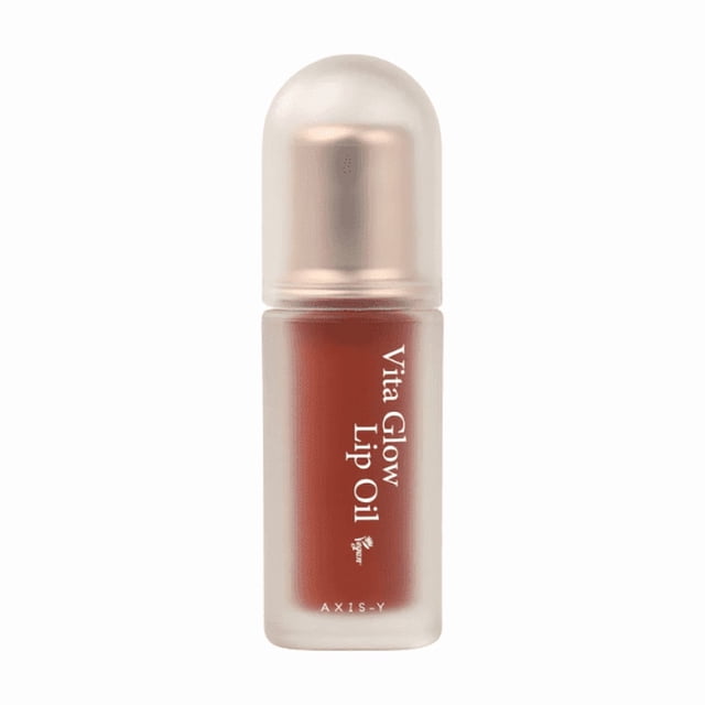 Axis-y Vita Glow Lip Oil 4.5g - Cozy Fig, a vegan lip treatment with a fig-inspired tint and glossy finish. The compact bottle features a frosted design with a rose-gold cap, containing a lightweight, non-sticky formula enriched with Vitamin E, Ceramide NP, and Panthenol for hydration and a luminous glow. Ideal for enhancing natural lip color and providing lasting moisture.
