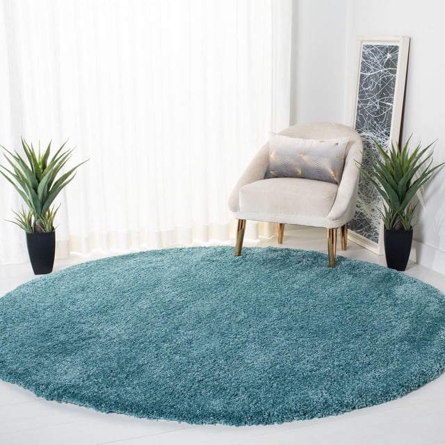 Safavieh Milan Harlow Tapis Shag Uni en Fil Shag Synthétique Rond Sarcelle, Ensemble dans une Pièce Lumineuse avec une Chaise en Velours beige avec des Pattes Dorées et un Coussin Décoratif, Entouré de Deux Plantes en Pot Vertes et d'Une Oeuvre Abstraite Encadrée Adossée au Mur, Convient pour Ajouter une texture Douce aux Espaces Contemporains.