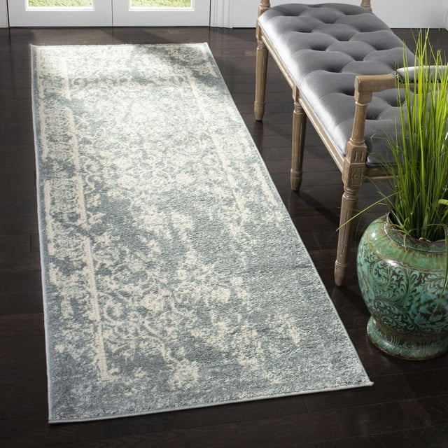 Safavieh Adirondack Zoey Traditional Faded Area Rug in muted blue and cream abstract pattern, power loomed from polypropylene yarns, placed on dark hardwood floor beside a wooden bench with gray tufted cushion and a green ceramic planter with tall grass, suitable as an accent rug for entryways or hallways.