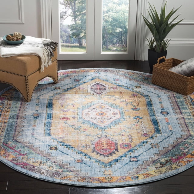 SAFAVIEH Bristol Leola Traditional Area Rug, a round accent rug with a distressed antique pattern in muted blue, yellow, and red tones made from durable polyester fibers, shown on dark hardwood flooring near a beige ottoman and woven basket with a plant, suitable for adding vintage charm to modern interiors.