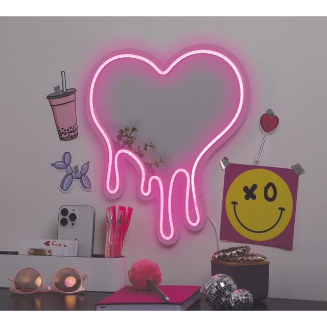 Merkury Innovations Miroir Cœur Néon à Goutte de 13 Pouces Alimenté par USB avec surface Miroirée Réflétant des Formes de Plantes Légères, LED Rose Luisant en Forme de Cœur Goutte à Goutte sur un Mur Blanc. décor Mural à Proximité Comprend des Autocollants de bubble tea et de Chien Ballon, une Affiche Visage Souriant avec « XO », et un Autocollant Sucette Cœur. sur le Bureau Dessous Se Trouvent des Stylos Roses, un Téléphone Intelligent, un Carnet Rose avec Stylo Duveteux, des Lunettes de Soleil Rondes Roses, et Deux Petites Boules disco. le Miroir Est Idéal pour l'Éclairage d'Ambiance