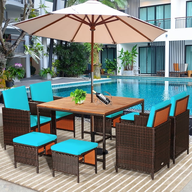 Costway 9PCS Patio Rattan Dining Set with turquoise cushioned chairs, ottomans, and a square acacia wood tabletop featuring an umbrella hole. Includes four armchairs, four ottomans, and a table made of weather-resistant PE wicker and a sturdy steel frame. Designed for compact storage, this set is perfect for patios, gardens, or poolside areas.
