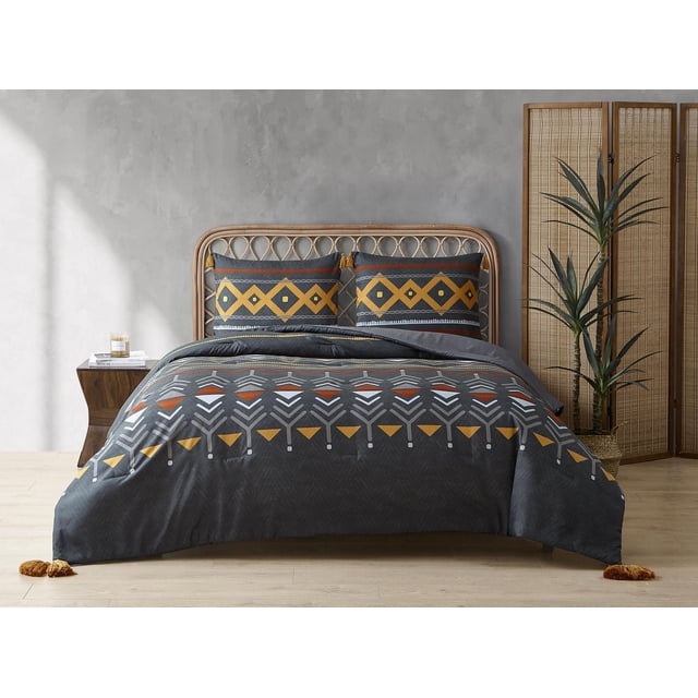 3 Piece Tapestry Comforter Set with a grey comforter featuring embroidered geometric patterns in mustard yellow, white, and rust orange, paired with matching pillow shams with diamond motifs and tassels, displayed on a rattan bed frame in a minimalist bedroom with light wood flooring and a woven room divider, ideal for enhancing bedroom warmth and style.