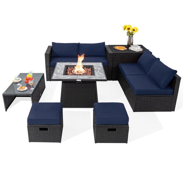 Patiojoy 9 Pieces Outdoor PE Rattan Wicker Sectional Sofa with 35-Inch Gas Fire Pit Table Space-Saving Patio Conversation Set with Storage Box Navy. This set includes a black PE rattan sectional sofa with navy cushions, a 35-inch gas fire pit table with a marble-pattern ceramic tabletop, a tempered glass coffee table, a storage box, two ottomans, two armless sofas, and two corner sofas. The fire pit table offers 50,000 BTU heat output with a simple ignition system for warmth and ambiance. The furniture is arranged in a U-shaped layout, emphasizing its space-saving design and ample seating. Decorative elements like a vase with flowers and serving dishes are displayed on the tables.