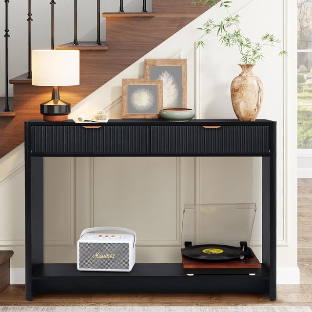WIRRYTOR Table Console avec Rangement en Noir, au design Moderne avec Deux Tiroirs, un Motif de Lattes de Bois Verticales sur la Porte Coulissante et des Poignées en Bois Élégantes. la Table Comprend un Plateau Spacieux, une Tablette Inférieure à Lattes et des Pieds en Bois Robustes. Exposée dans un Salon Près d'Un Escalier, Elle Contient des Objets Décoratifs, une Lampe et un Tourne-Disque.