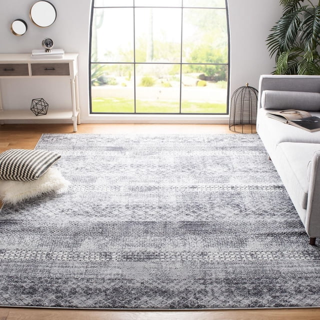 SAFAVIEH Amelia Manuel Distressed Southwestern Area Rug in grey with plush synthetic yarn and a textured distressed southwestern pattern, on a hardwood floor in a bright living room with a grey sofa, pillows, white console table, and large window, also suitable for bedrooms or family rooms.