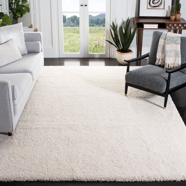 Safavieh California Tapis Shag Uni en Peluche Présentant une pile Shag Blanche en Polypropylène dense de 4,5 Kg/m2 dans un Salon avec des Planchers de Bois Franc Sombres, un sofa Gris Pâle et un Fauteuil Noir avec un Jeté, Près des Portes Françaises s'Ouvrant sur une Vue Extérieure Verte, Convient pour Ajouter Douceur et Chaleur en Peluche aux Espaces de la Maison.