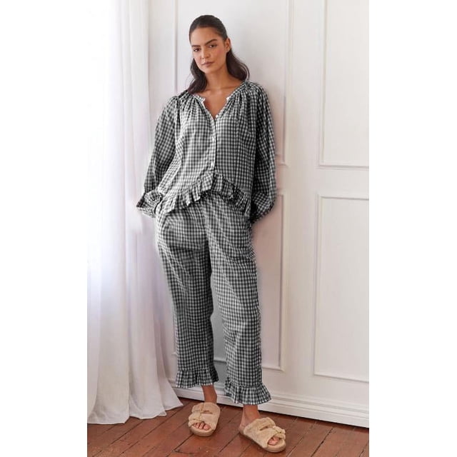 Gupgi Women Plaid Pajama Sets 2 Piece Lounge Set featuring a long sleeve button-down shirt with ruffled hem and matching ruffle-trimmed pants. The set is made of 95% polyester and 5% elastane, offering a soft and comfortable fit. The plaid pattern is multicolored, suitable for lounging or sleeping. Displayed in a relaxed indoor setting with wooden flooring and white curtains.
