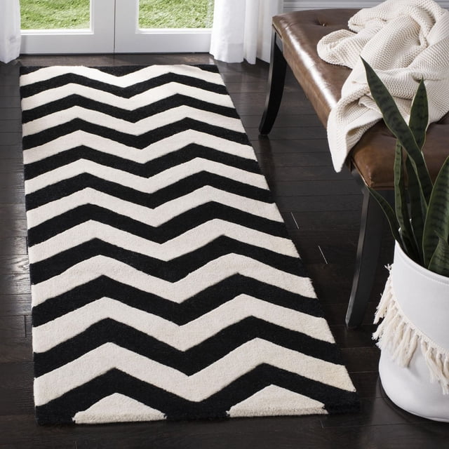 Safavieh Chatham Jake Tapis à Rayures Zigzag avec construction en Laine Tuftée à la Main Présentant des Rayures Zigzag Noires et Blanches, Placé sur un Plancher de Bois Franc Foncé à Côté d'Un Banc en Cuir Brun avec un Jeté en Tricot Crème et une Plante Serpent dans un pot à Franges Blanc, Idéal pour une Utilisation Contemporaine comme Tapis d'Accent et une Douceur de Poil Moyenne sous les Pieds.