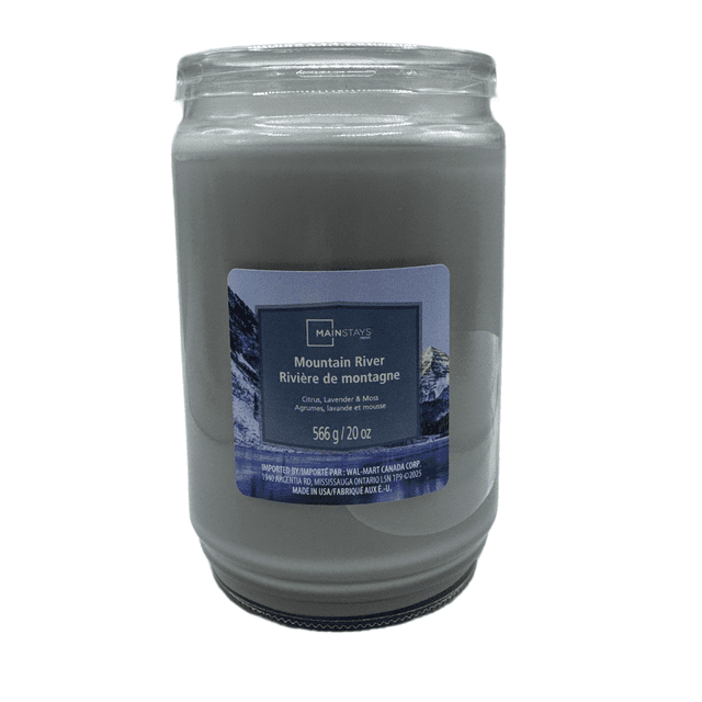 MAINSTAYS PL Mountain River Scented Single-Wick Glass Jar Candle, 20 oz, with grey paraffin wax in a clear glass jar and a blue label showing mountain scenery. The fragrance combines citrus, lavender, and moss, suitable for home décor and creating a relaxing atmosphere.