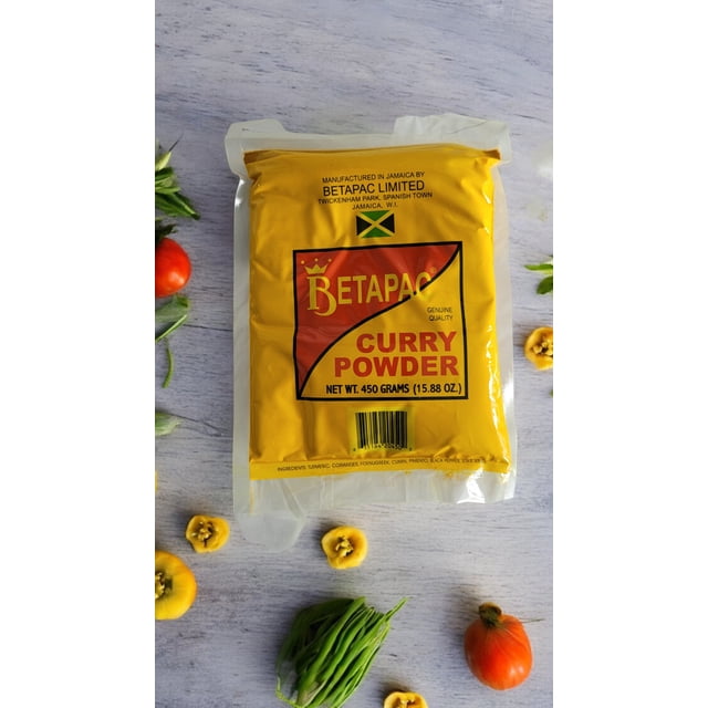 Betapac Jamaican Curry Powder (450g) in a bright yellow package with bold red and black text, displaying the Jamaican flag and branding. The package is set on a light wooden surface surrounded by fresh ingredients like tomatoes, green beans, and sliced yellow peppers, highlighting its versatility in Caribbean cuisine.