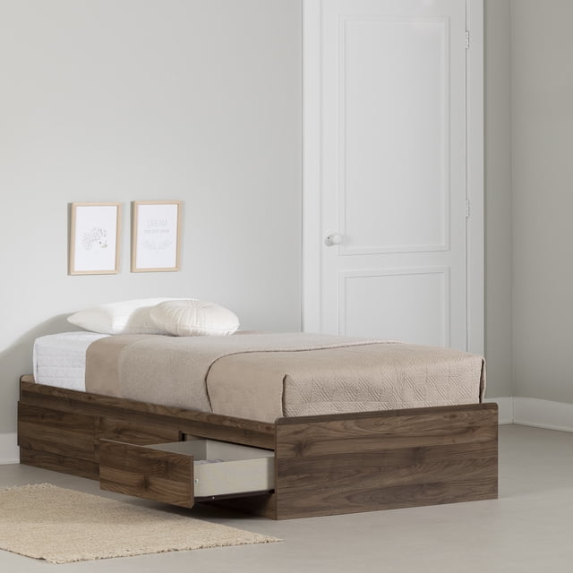 South Shore Yodi Lit Simple avec 3 Tiroirs en Fini Noyer Naturel, un Lit Plateforme de Style Scandinave avec Trois Grands Tiroirs sous le Lit sur Glissières en Métal, un Tiroir s'Ouvrant Montrant l'Espace de Rangement. le Lit Est Habillé de Literie beige et d'Oreillers, Adossé à un Mur Gris Pâle avec Oeuvre Encadrée et une Porte Blanche dans une Chambre Minimaliste.