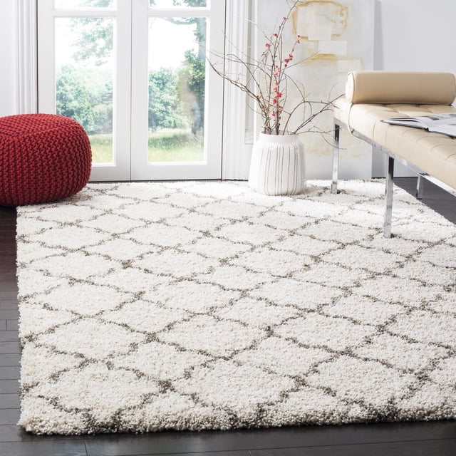 Safavieh Hudson Jaye Shag Géométrique Tapis en Ivoire avec Motifs de Carreaux en Forme d'Oignon Gris sur un Épais Poil Shag Moelleux, Posé sur des Planchers de Bois Franc Sombres dans une Pièce Moderne avec un pouf Tricoté Rouge, vase en Céramique Blanc avec branches Nues, et un Banc en Cuir beige avec Pattes Chromées, Convient pour Ajouter de la texture à un décor Urbain Ou Contemporain.