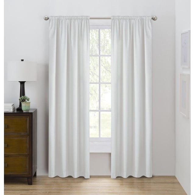 Eclipse Draft Stopper 63" room darkening rod pocket window curtains panel in white, hanging on a silver curtain rod in a bright room with light wood flooring and white walls, featuring insulating fleece fuse backing to block cold air and light for energy efficiency.