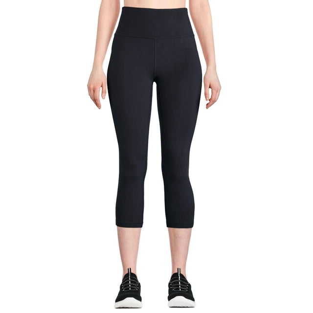 Athletic Works Women's High Rise Capri in black, front view on a model. Features a wide elasticized waistband, high-rise fit, and capri length below the calf. Made from breathable interlock knit with DRI-MORE moisture-wicking technology and a hidden back pocket for small essentials. Suitable for yoga, cardio, and casual activewear.