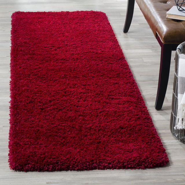 Safavieh California Solid Plush Shag Area Rug in deep red with a super dense 4.5kg/m² polypropylene pile, shown on light wood flooring beside a brown leather bench and a basket with a blanket, ideal for adding plush softness and warmth to home spaces.