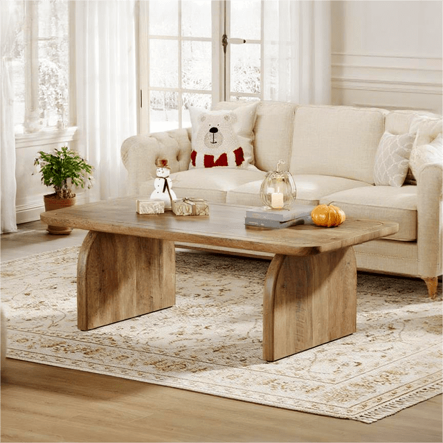Fnova Farmhouse Coffee Table for Living Room, a 47.24-inch rectangular wood coffee table with a mid-century farmhouse design. The table features a 1.57-inch thick tabletop and sturdy legs, supporting up to 220 lbs. It has a smooth, waterproof, and scratch-resistant surface, complemented by rounded edges for safety. The table is shown in a cozy living room setting with a beige sofa, decorative pillows, and a patterned rug, enhancing the minimalist and elegant decor.