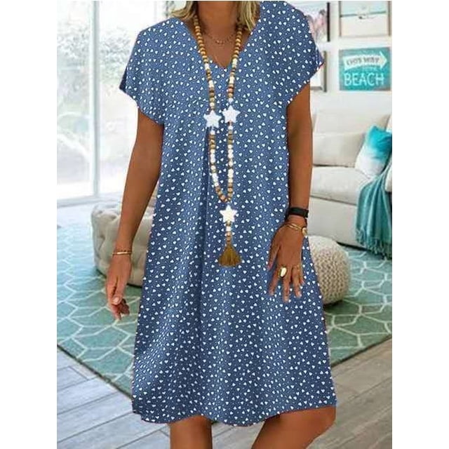 Robe pour Femmes Grande Taille Tendance 2024 à Coupe Ample et Décontractée avec Manches Courtes et Imprimé Estival. la Robe Est Présentée en Bleu avec un Petit Motif floral Blanc, Stylée avec un long Collier Perlé. Idéale pour les Sorties à la Plage Ou les Tenues Estivales Décontractées, la Robe Est Exposée dans un Décor Intérieur Lumineux à Thème Côtier.