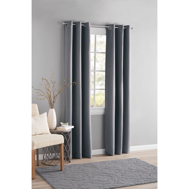 MAINSTAYS Blackout Energy Efficient Grommet Window Curtains Panel in dark grey with metal grommets on a silver rod, blocking light from a window in a modern room with light grey walls, beige chair, decorative side table with white vase and twig branches, and textured grey rug on wood flooring, ideal for privacy and energy savings.