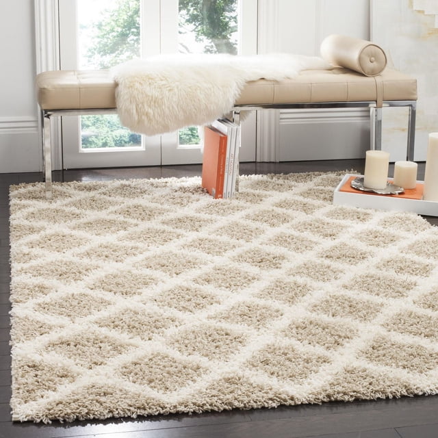 Safavieh Layla Geometric Plush Shag Area Rug with beige and cream diamond pattern, dense synthetic fibers, shown on dark hardwood floor beneath a beige leather bench with chrome legs in a bright room, ideal for high traffic areas and contemporary decor.