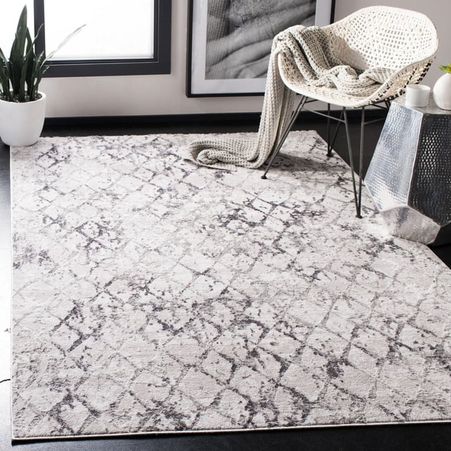 SAFAVIEH Amelia Roslyn Abstract Distressed Area Rug featuring a plush synthetic yarn texture with a light base and dark abstract geometric pattern, laid on a dark floor in a modern room with a white woven chair draped with a knitted throw, a metallic side table, and a potted plant by a window, suitable for living or bedroom accent.