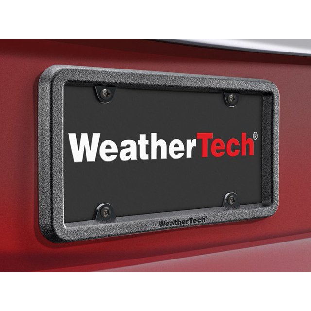 Weathertech License Plate Frame 8ALPBF1 BumpFrame with WeatherTech logo, shown in a black satin textured finish. The frame is made of 3/4-inch thick soft bumper material molded over high-impact polycarbonate, providing impact resistance and protection for the vehicle's front bumper. Designed without illumination, it features a robust and virtually unbreakable construction, ideal for preventing scratches and bumps. Frame only, mounted on a red vehicle.