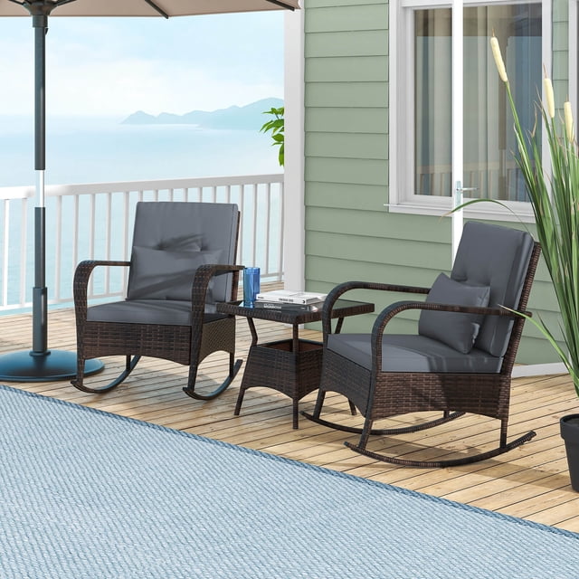 Costway 3 PCS Rocking Bistro Set with Removable Cushions & Tempered Glass Top Coffee Table in grey, featuring two rocking chairs with mix brown PE rattan frames, grey cushions, and lumbar pillows. Includes a matching coffee table with a tempered glass top secured by suction cups. The set is displayed on a wooden deck with a coastal backdrop, ideal for outdoor spaces like patios, porches, or gardens.