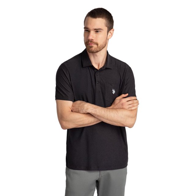 U.S. Polo Assn. Men's Solid Interlock Short Sleeve Polo in black with a classic collar, three-button placket, and chest pocket embroidered with the white U.S. Polo Assn. logo, made from breathable interlock fabric, shown front-facing paired with grey pants, suitable for warm weather wear.