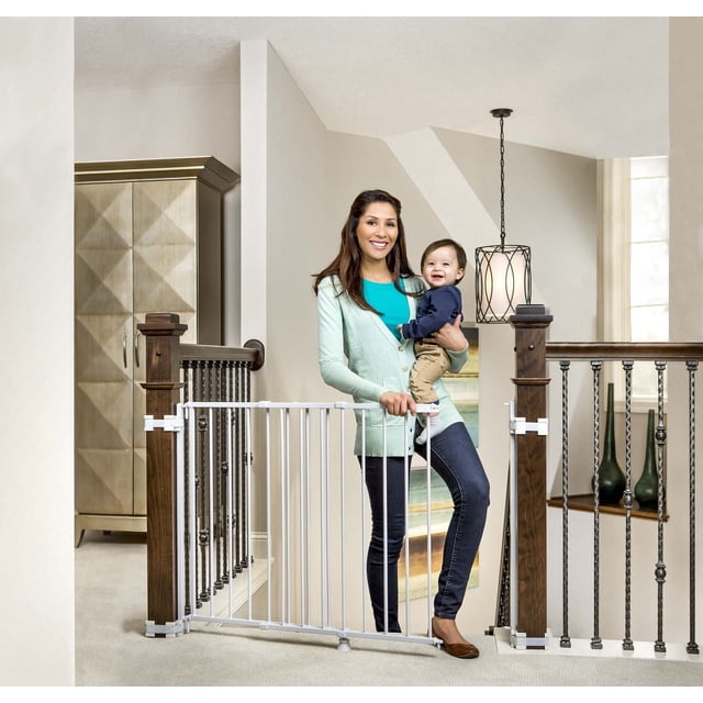 Regalo Baby Gate en Haut d'Escalier avec Cadre en Acier Blanc Installé entre des Rampes en Bois Foncé et des Barreaux en Métal Noir, Se Balançant dans les Deux Sens avec une Poignée à Loquet Facile. Positionné en Haut d'Escalier dans une Maison Lumineuse avec des Murs Neutres et un Décor Moderne.