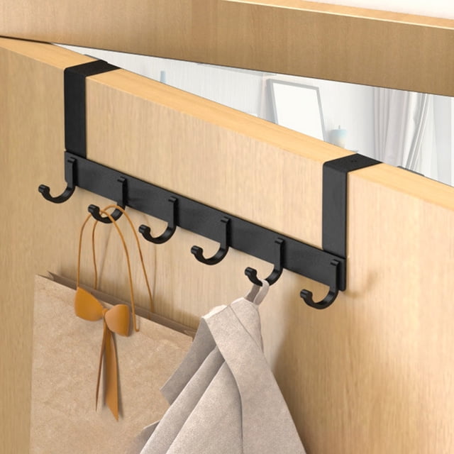 TIMIFIS Hooks for Hanging Six Hook Door Hook without Punch Door Traceless Door Back Rack Clothes Hanger. A black aluminum six-hook rack designed for over-the-door use, shown installed on a wooden door. The hooks are evenly spaced and used to hang a beige coat and a brown shopping bag. The traceless design ensures no damage to the door, and the compact size maximizes space utilization. Suitable for bedrooms, bathrooms, or kitchens.