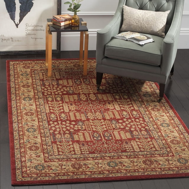 Safavieh Mahal Phylliss Traditional Area Rug showcasing classic Persian floral and geometric patterns in red and beige, power-loomed polypropylene for durability in high traffic areas, placed under a green upholstered armchair and beside a gold-legged side table with books and a plant, suitable for adding traditional elegance to living rooms or reading nooks.