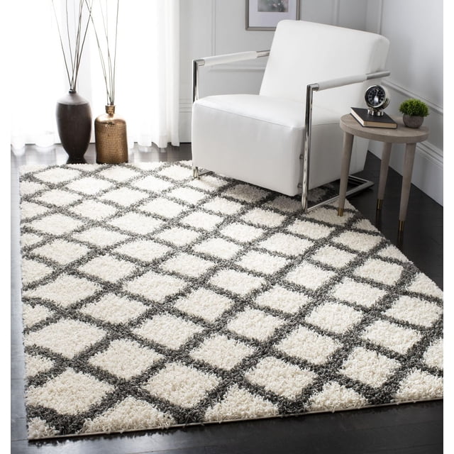 Safavieh Dallas Jerrie Tapis Shag Géométrique Présentant une surface Shag Blanche Pelucheuse avec Motif Losanges Gris Foncé, Placé sur un Plancher de Bois Franc Foncé sous un Fauteuil Moderne Blanc avec Accoudoirs Chromés et une Petite table d'Appoint Ronde avec des Articles Décoratifs, Idéal pour les Espaces à Fort Passage à la Maison Ou au Bureau.