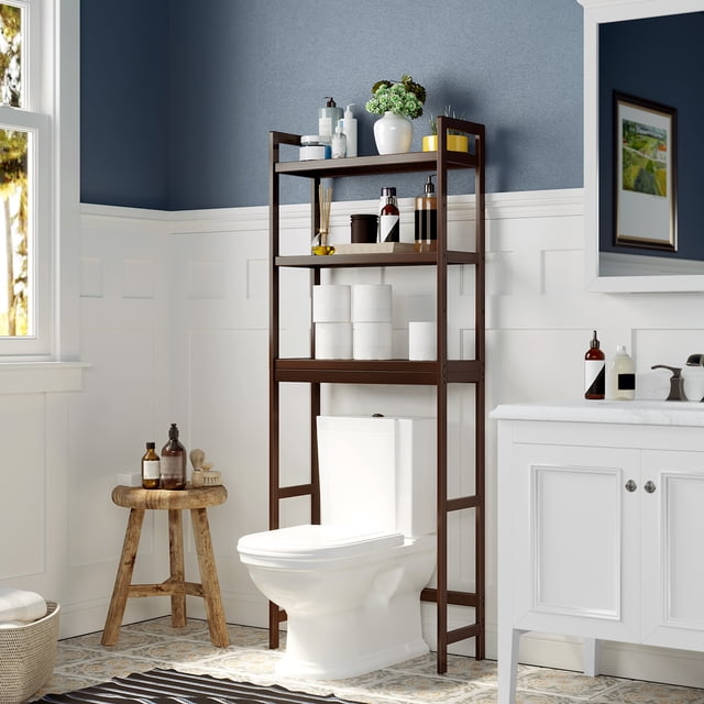SONGMICS Over-The-Toilet Storage Bathroom Organizer Toilet Rack with Adjustable Shelf, Brown UBTS01BR. A 3-tier bamboo storage rack in a brown finish, designed to fit over a toilet. It features adjustable shelves, hooks, and a toilet paper holder, ideal for organizing toiletries, towels, and decor. Shown in a bathroom with white wainscoting and a blue wall, the rack measures 10.2"D x 24.8"W x 66.9"H and is suitable for bathrooms, laundry rooms, or kitchens.