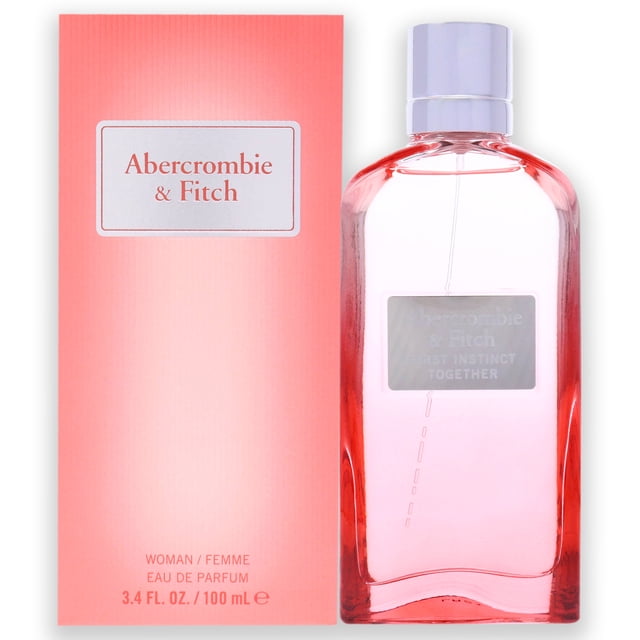 Abercrombie & Fitch First Instinct Ensemble Femmes 3,4 oz Vaporisateur EDP Montré aux Côtés de Son Emballage aux Tons Corail. la Bouteille a un design Épuré et transparent avec une Teinte Rose Douce, une Étiquette Argentée et un Bouchon Métallique. Cette Eau de Parfum Offre un Parfum Rafraîchissant, oriental et Boisé, Parfait comme Parfum pour Femmes pour Diverses occasions.