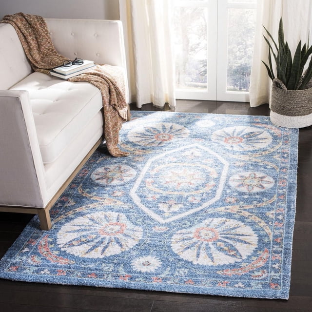 Safavieh Saffron Jaslyn Bordered Oriental Area Rug in blue with distressed cotton texture and circular floral medallion patterns, bordered edges, placed on dark hardwood floor beside a white tufted sofa with a brown knitted throw and books, near sheer curtains and a woven basket holding a tall green snake plant, suitable for adding warmth and colour to living spaces.