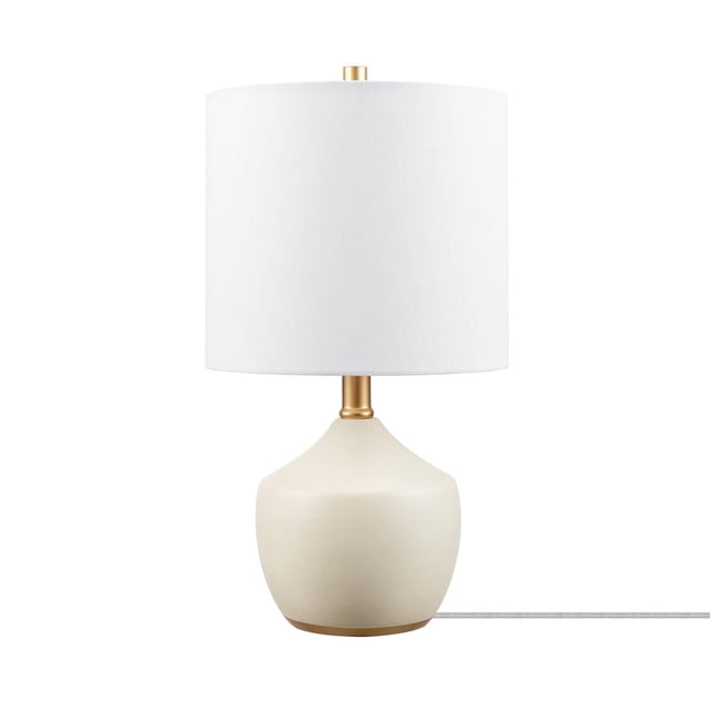Novogratz x Globe 16" cream finish concrete textured ceramic table lamp with a rounded base, brass accents, and a white linen cylindrical shade, featuring a 6-foot clear cord for flexible placement in home lighting setups.