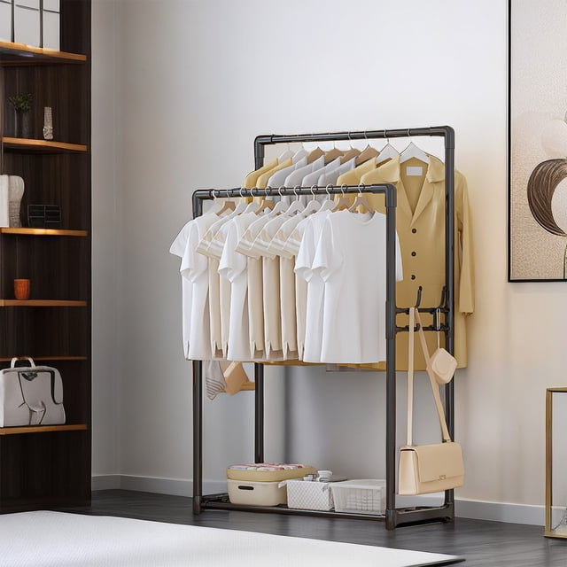 Dvkptbk Coat Rack Double Pole Clothes Hanger featuring a multifunctional design with two poles for hanging clothes, a sturdy iron frame in black, and a bottom storage area for boxes or shoes. The rack is shown in a modern bedroom setting, holding white and beige clothing, with additional storage boxes placed at the bottom.