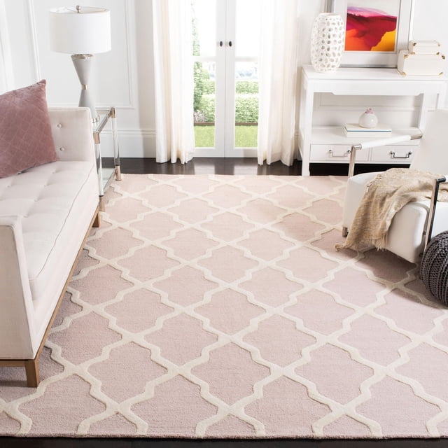 Safavieh Cambridge Liam Tapis Géométrique pour Aire en Rose Pâle avec Motif Treillis Blanc Cassé, Tapis d'Accent en Laine Tufté à la Main dans un Salon Éclatant Comprenant un sofa beige avec Coussin mauve, un Fauteuil Blanc avec Jeté beige, une table console Blanche et des Portes en Verre avec des Rideaux Blancs.