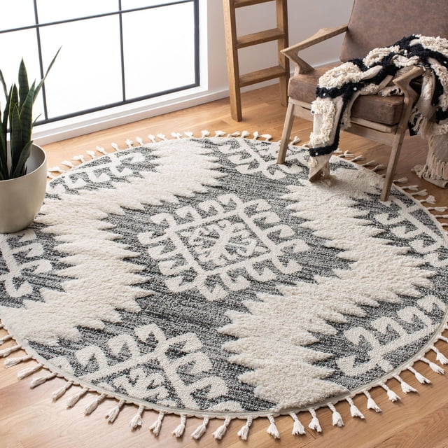 Safavieh Moroccan Tassel Shag Desmond Southwestern Area Rug, round with plush synthetic yarns, featuring a tribal southwestern cream and charcoal pattern with tassel fringe, placed on hardwood flooring beside a brown armchair and potted snake plant, ideal for adding warmth and texture to living areas.