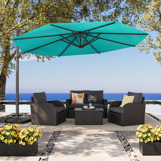 CorLiving 11.5ft Deluxe Tilting and Rotating Offset Patio Umbrella with Aluminum Frame and Durable Turquoise Canopy, shown open above a dark grey woven outdoor seating set with cushions and colorful pillows on a beige rug by a pool with ocean view, surrounded by trees and yellow flowering planters, suitable for adjustable shade in outdoor living areas.