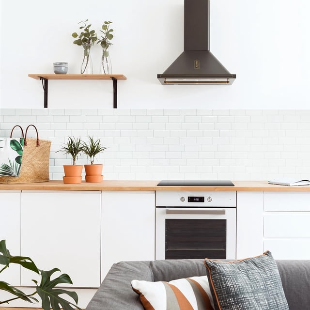 SMART TILES PEEL & STICK BACKSPLASH - METRO CAMPAGNOLA - 4 Pieces 11.56 x 8.38 white peel and stick subway tile backsplash installed on a kitchen wall with wooden countertop, white cabinetry, black range hood, and terracotta potted plants, ideal for quick DIY kitchen or bathroom updates.