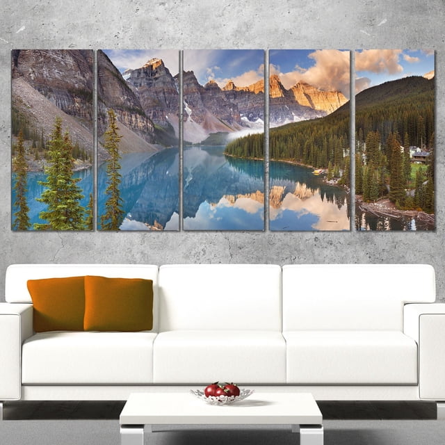 Design Art Lac Moraine dans le Parc Banff Canada Impression sur Toile d'Art de Paysage Mettant en Vedette une Toile Enveloppante à Cinq Panneaux avec une image Haute Résolution de Lac Moraine turquoise Réflétant des Pins et des Sommets de Montagne Rugueux au Coucher du Soleil, Exposée au-Dessus d'Un sofa Blanc avec des Coussins orange dans un Salon Moderne.