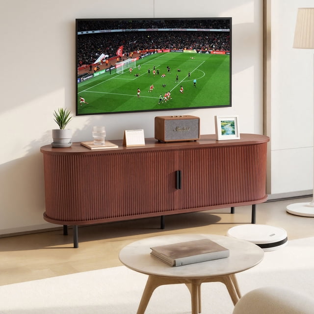 VEVOR TV Stand, Boho Entertainment Center for TVs up to 58 inches, ideal for living rooms and bedrooms. The brown stand features a slatted door frame, adjustable storage shelves, rolling doors, and cable management. Positioned beneath a wall-mounted TV showing a soccer match, it is decorated with a speaker, plant, and picture frame on top.
