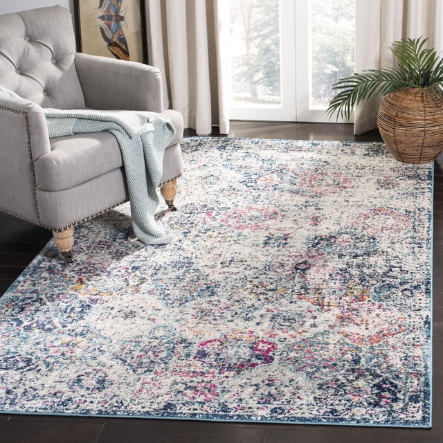 SAFAVIEH Madison Tapis Géométrique Floral Judith Mettant en Vedette un Motif Floral Vieilli en Bleu, Rose et Jaune sur un Fond Clair, Posé sur des Planchers de Bois Franc Sombres dans une Pièce Lumineuse, Partiellement sous un Fauteuil Rembourré Gris avec des Pattes en Bois et un Jeté Tricoté Bleu Pâle, des Rideaux Près du beige et un Panier Tissé avec un Feuillage Vert, Idéal pour Rehausser la Déco de la Maison de Transition.