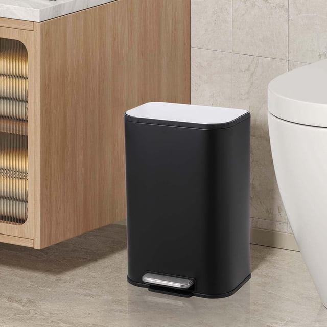 Stainless Steel Trash Can with Lid – 3.2 Gallon Step-On Garbage Bin with a compact rectangular design in black and polished finish. Features a soft-close lid, hands-free foot pedal, and removable inner bucket for efficient waste disposal. Ideal for use as a wastebasket in kitchens, bathrooms, or offices. Displayed in a modern bathroom setting next to a toilet and wooden cabinet.
