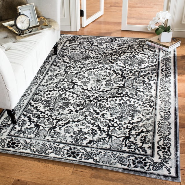 Safavieh Evoke Tapis Traditionnel Lorna avec Motif floral et de Vigne Noir et Gris sur Fond Clair, Tissé Mécaniquement à Partir de Fils de Polypropylène à Haute Torsion pour la Durabilité et l'Entretien Facile, Montré sur un Plancher de Bois Franc à Côté d'Un sofa beige et d'Une Pile de Livres avec une Orchidée Blanche, Convient comme Tapis d'Accent Stylé pour les Intérieurs de la Maison.