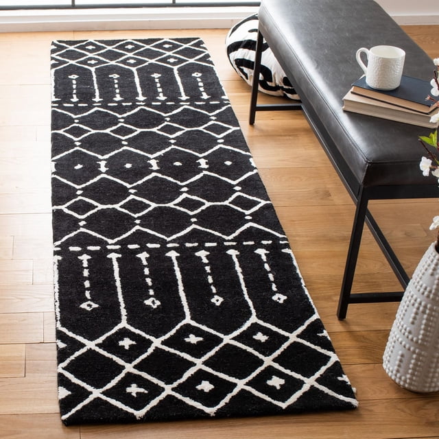 Safavieh Himalaya Darin Geometric Area Rug in black with white geometric diamond and linear patterns, made from 100% hand-loomed wool, placed on light hardwood flooring beside a black leather bench with books and a white mug, suitable as a durable runner rug for modern home decor.