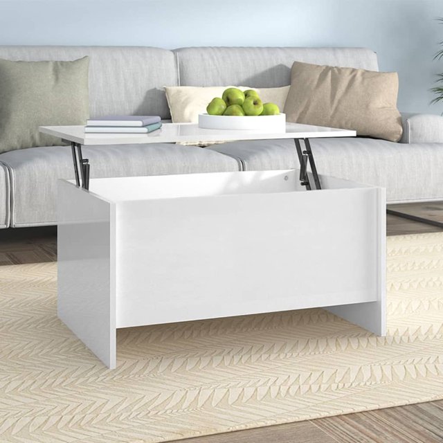 vidaXL Coffee Table High Gloss White 80x55.5x41.5 cm made of engineered wood, featuring a lift-top design for adjustable height and a hidden storage compartment. The table is shown in a modern living room setting with a beige patterned rug, a grey sofa, and decorative items like a fruit bowl and books on the tabletop.