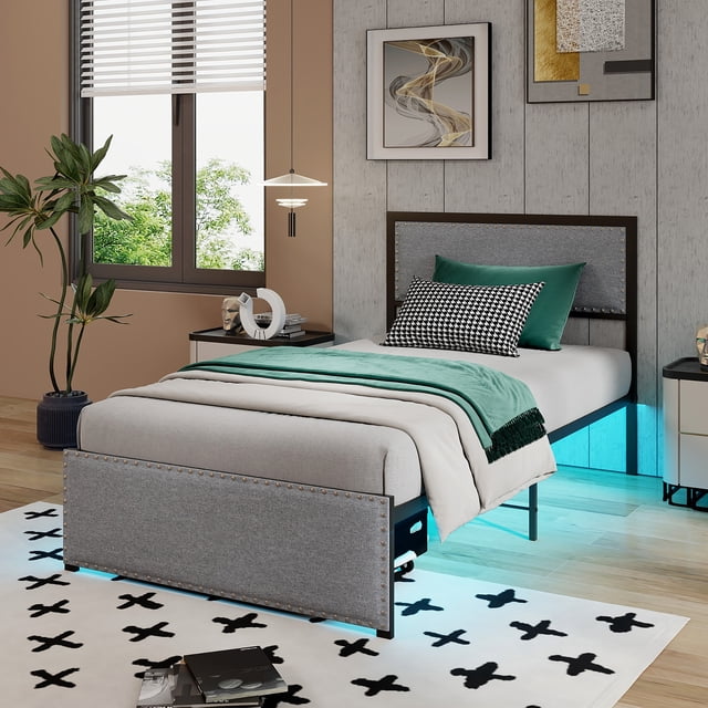 Gymax Cadre de Lit Format Simple avec Tiroir de Rangement et Lumières DEL, Doté d'Une Tête de Lit Grise Rembourrée avec Garniture de Clous Décoratifs et d'Un design Moderne. le Lit Comprend une Bande Lumineuse DEL RVB en Dessous, Offrant des Couleurs et des modes Personnalisables Contrôlés via une Application Ou une Télécommande. un Tiroir de Rangement Roulant Est Niché sous le Lit pour une Organisation Accrue. la Plateforme Métallique Robuste Élimine le Besoin d'Un Sommier et Supporte jusqu'à 1000 Lb. Présenté dans un Cadre de Chambre Contemporain avec des accents Décoratifs et une Lumière Naturelle.