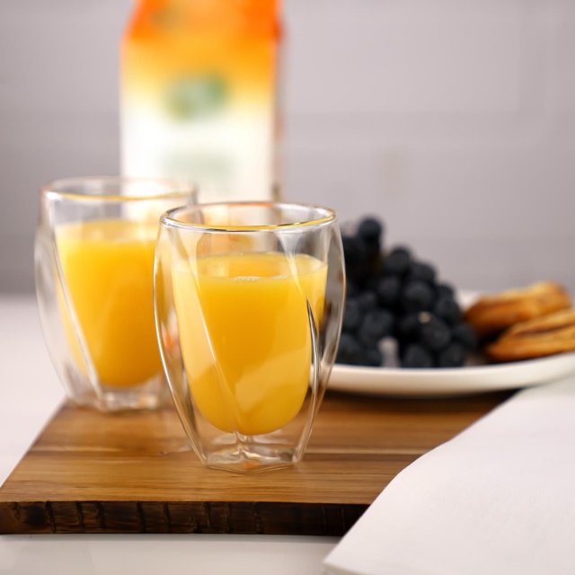 Verre Double Double Torsion, 300 ml Ensemble de 2, Verres Transparents à Double Paroi avec arcs de Torsion Remplis de Jus d'Orange, Placés sur une Planche en Bois avec des Raisins et des Craquelins en Arrière-Plan, Conçus pour Garder les Boissons Isolées et Sans Condensation, Convenant Aussi aux Boissons Chaudes Ou Froides.